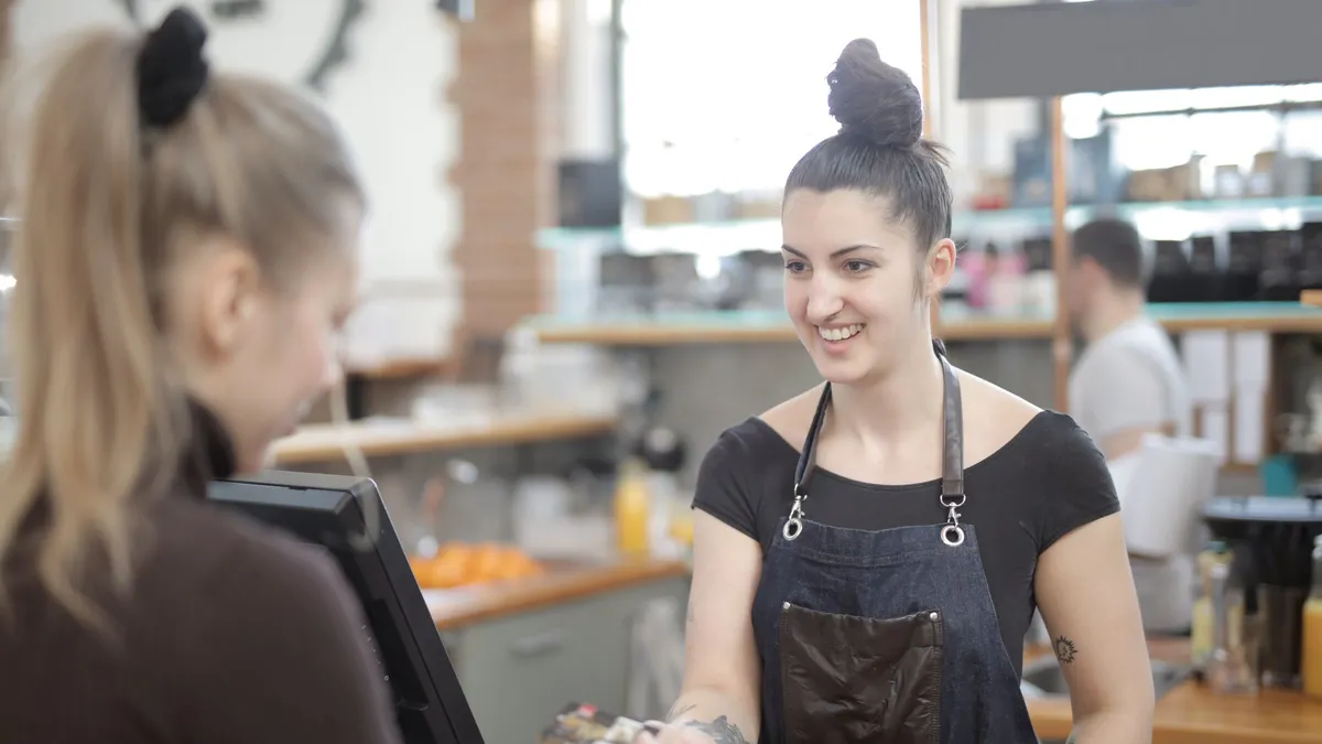 Barista taking a card payment at a cafe counter, the small everyday purchase that should never be the reason for a $100 payday loan