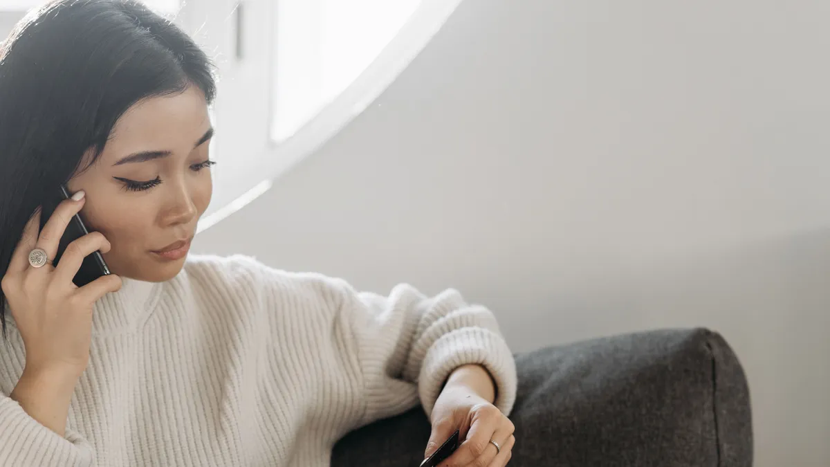 Woman on the sofa talking to a lender on the phone with her bank card in hand, asking for a smaller amount than the $100 payday loan form offered