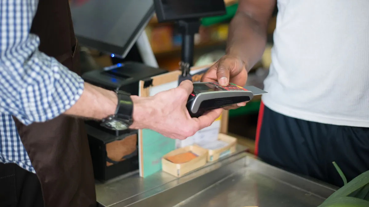 Customer tapping a bank card at a store terminal, the kind of small purchase a $100 payday loan is usually too expensive for
