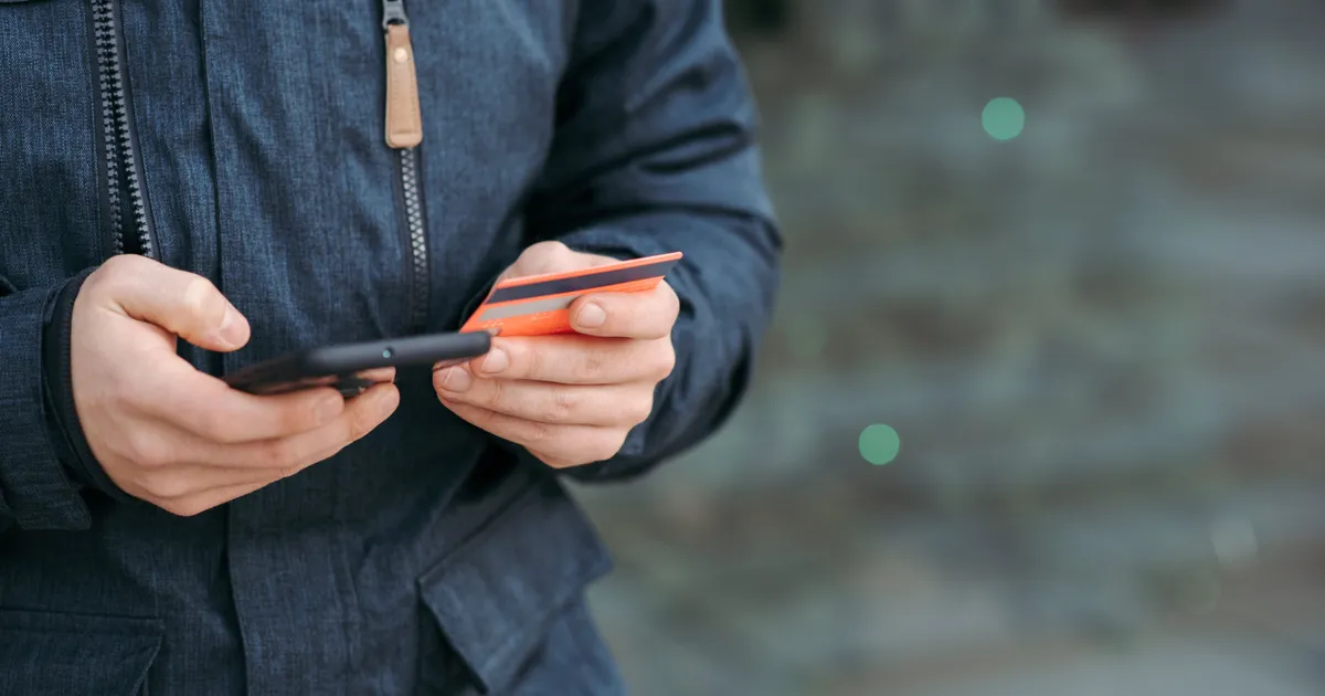 Man entering his details on his phone with his bank card in hand to apply for a $300 payday loan in Canada