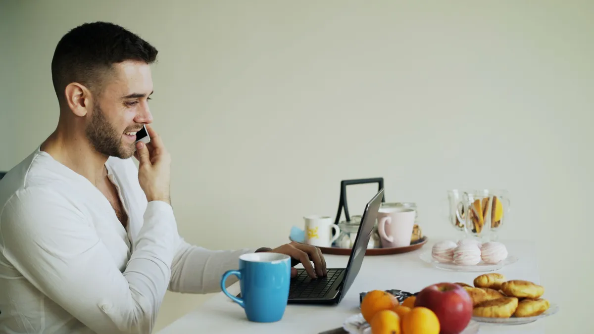 Man checking what a $300 payday loan costs on his phone and laptop over breakfast