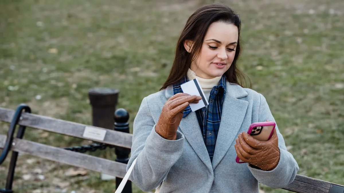 Woman on a park bench reading the e-Transfer notice for her $300 payday loan on her phone