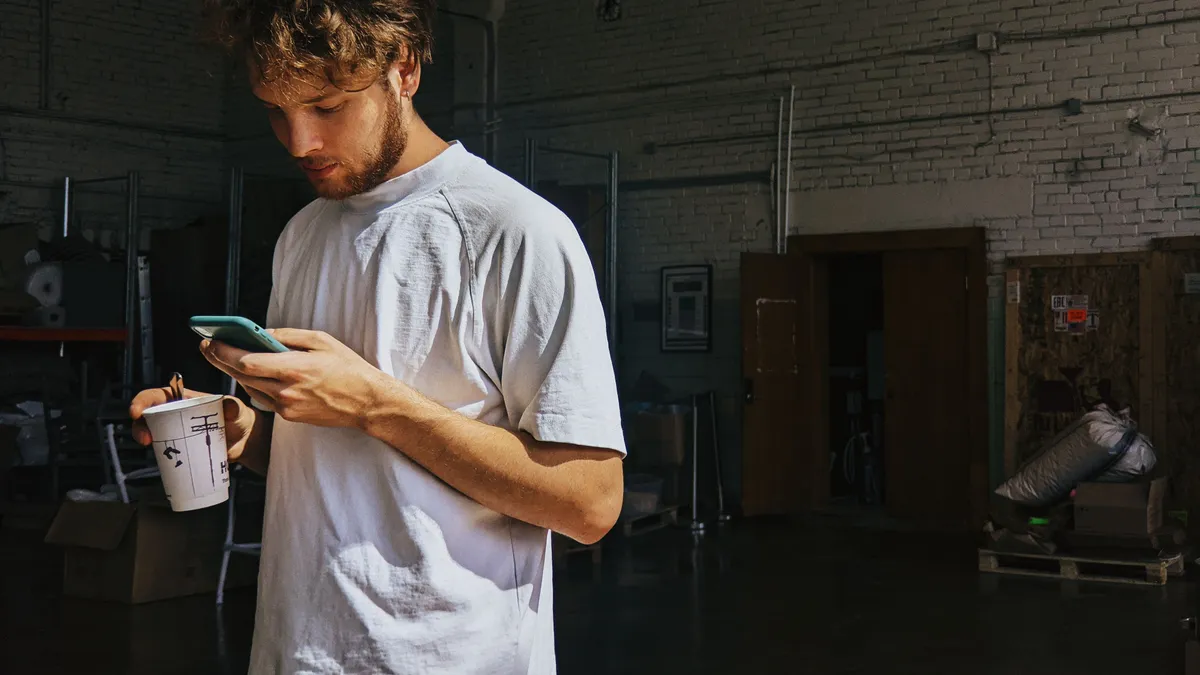 Part-time warehouse worker on a coffee break checking his $300 payday loan application on his phone