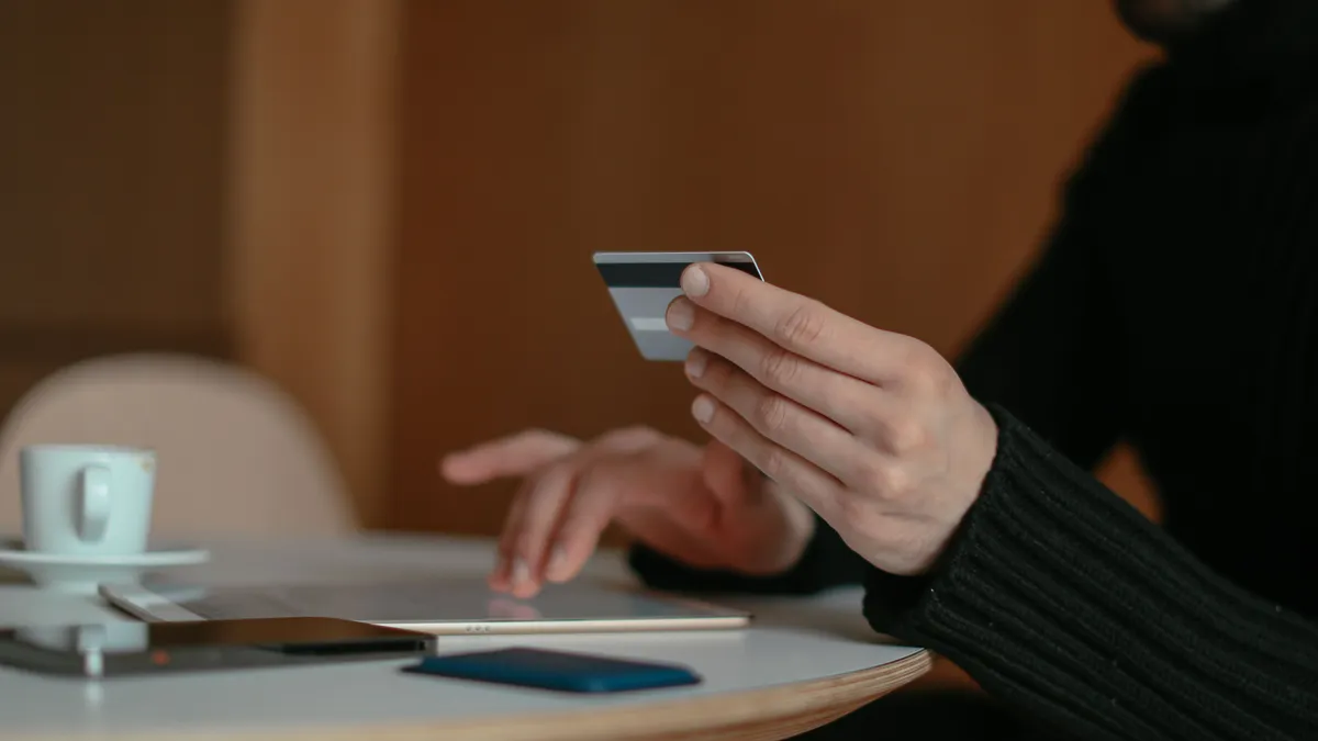 Man holding his bank card over a tablet at a cafe table, checking whether a $500 payday loan fits his next paycheque