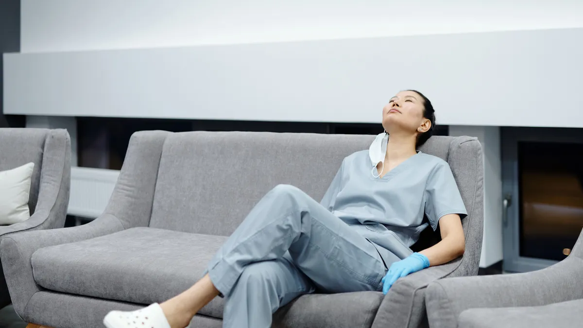 Nurse in scrubs resting on a couch after a shift, the paycheque a $500 payday loan is repaid from