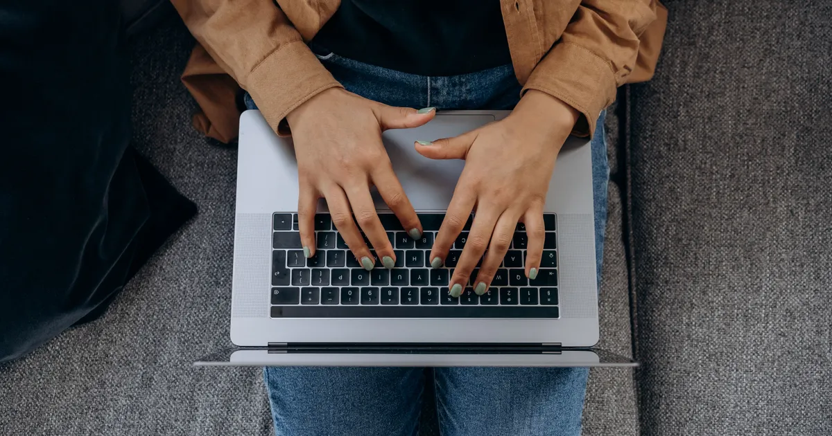 Hands typing a payday loan application on a laptop while sitting on the sofa