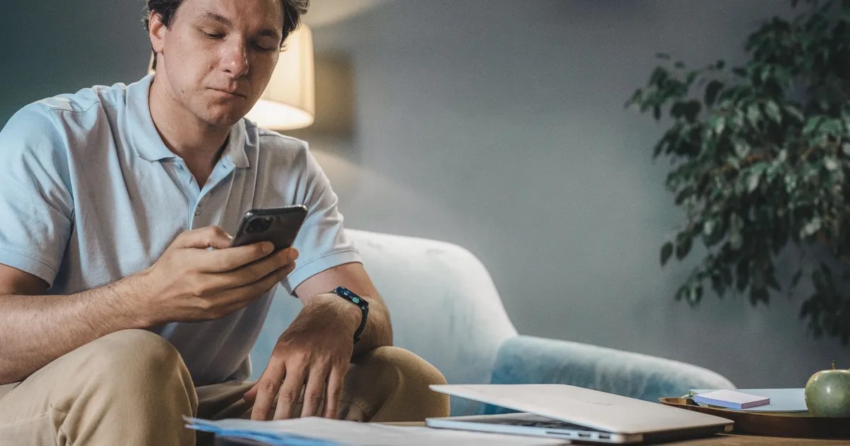 Man on his sofa at the weekend checking a bill and his bank balance on his phone