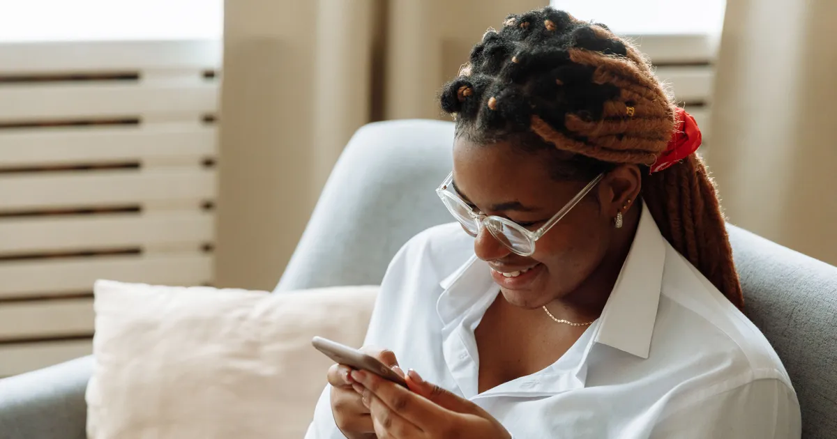 Woman relaxing on her sofa smiling as she reads a loan decision on her phone